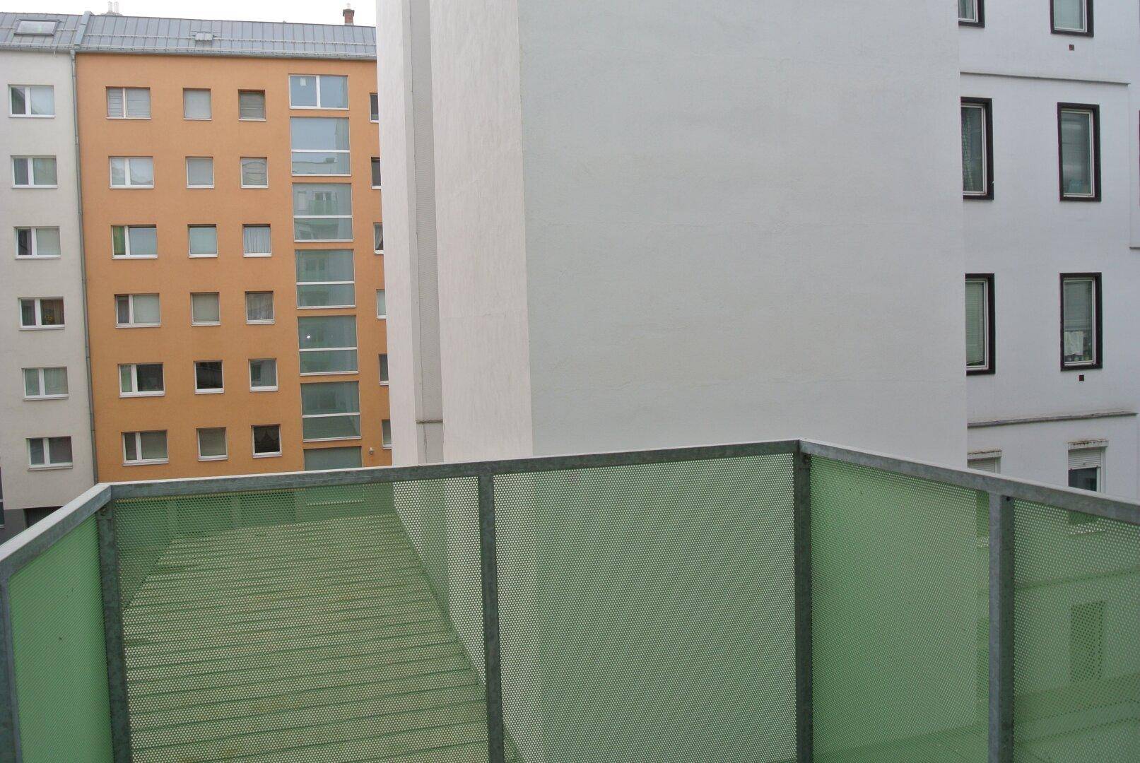 Blick von einem Balkon mit grüner Brüstung auf umliegende Wohngebäude.
