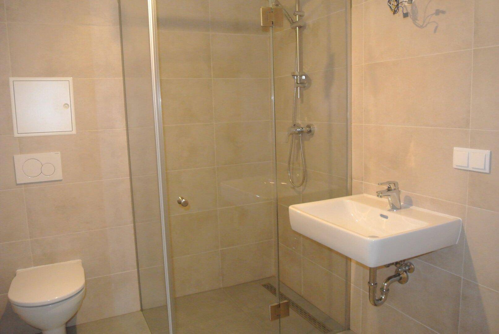 Modernes Badezimmer mit beigefarbenen Fliesen, ebenerdiger Dusche und wandhängendem WC.