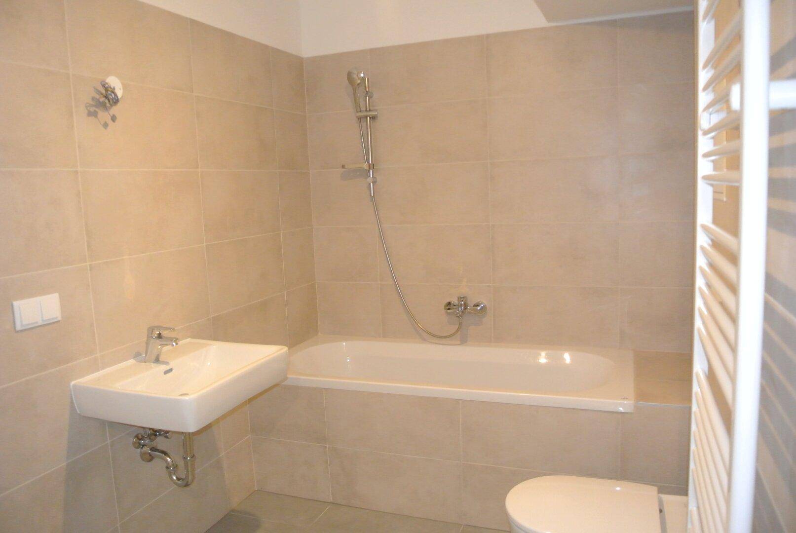 Modernes Badezimmer mit beigefarbenen Fliesen, Badewanne, Waschbecken und beheiztem Handtuchhalter.