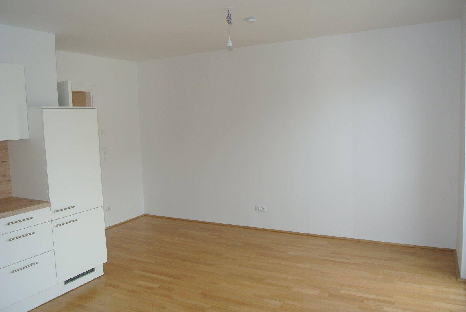 Heller Wohnbereich mit weiß gestrichenen Wänden und einem warmen Holzparkettboden.