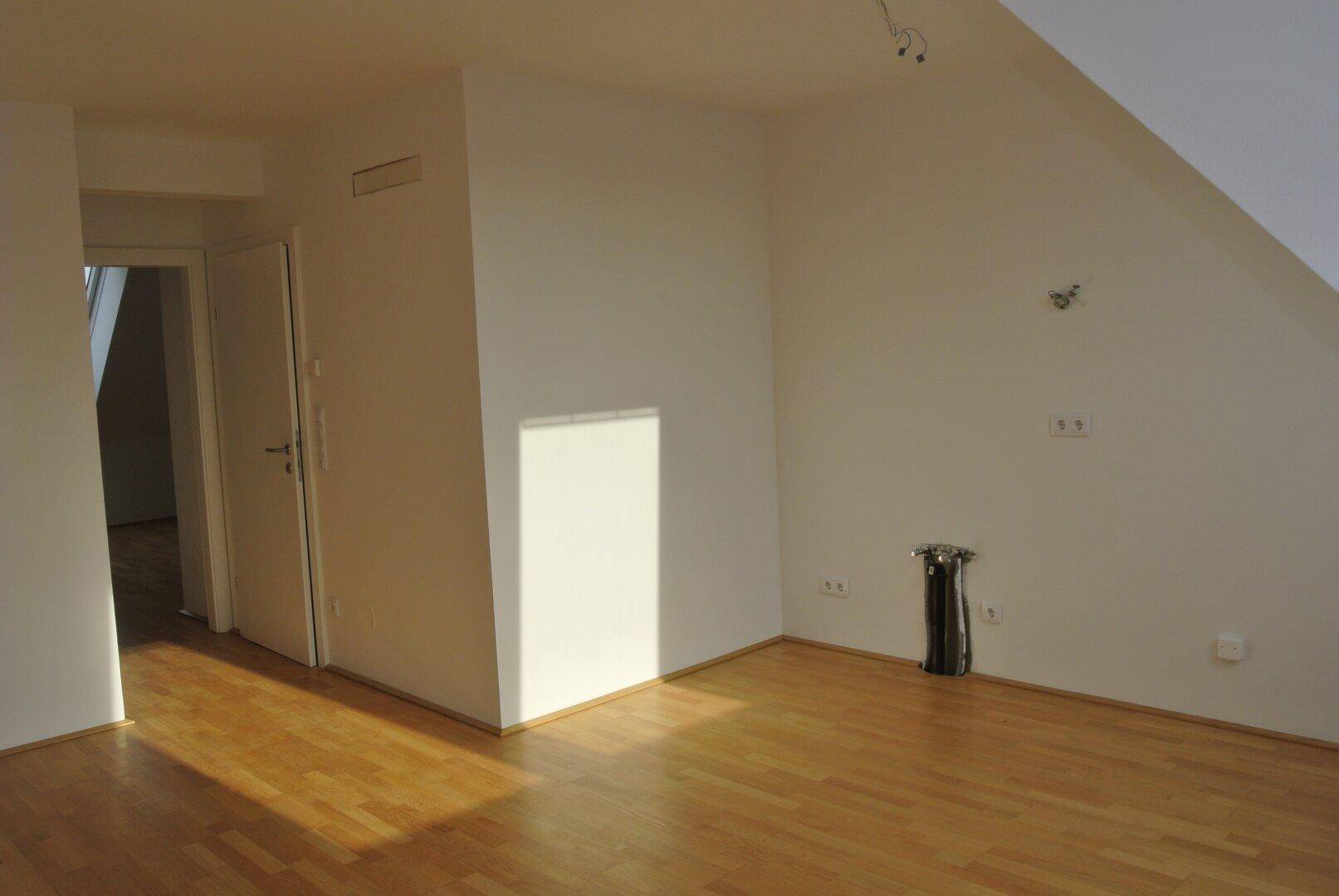 Leerer Raum mit Holzfußboden, weißen Wänden und Zugang zu einem weiteren Zimmer.