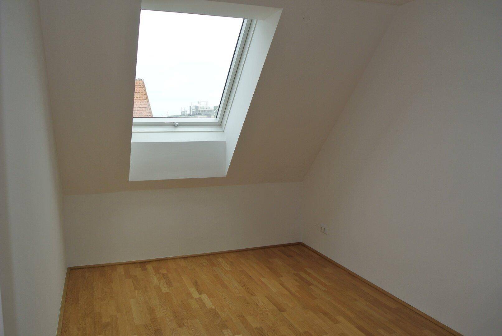 Heller Raum im Dachgeschoss mit Holzfußboden und großem Dachfenster.