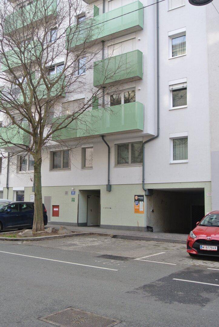 Wohnhausfassade mit grünen Balkonen, einem Baum und einem geparkten roten Auto.