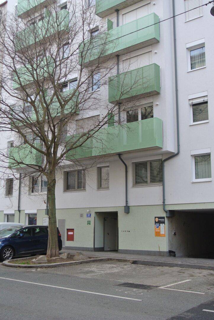 Wohngebäude mit grünen Balkonen, Eingangsbereich und einem kahlen Baum davor.