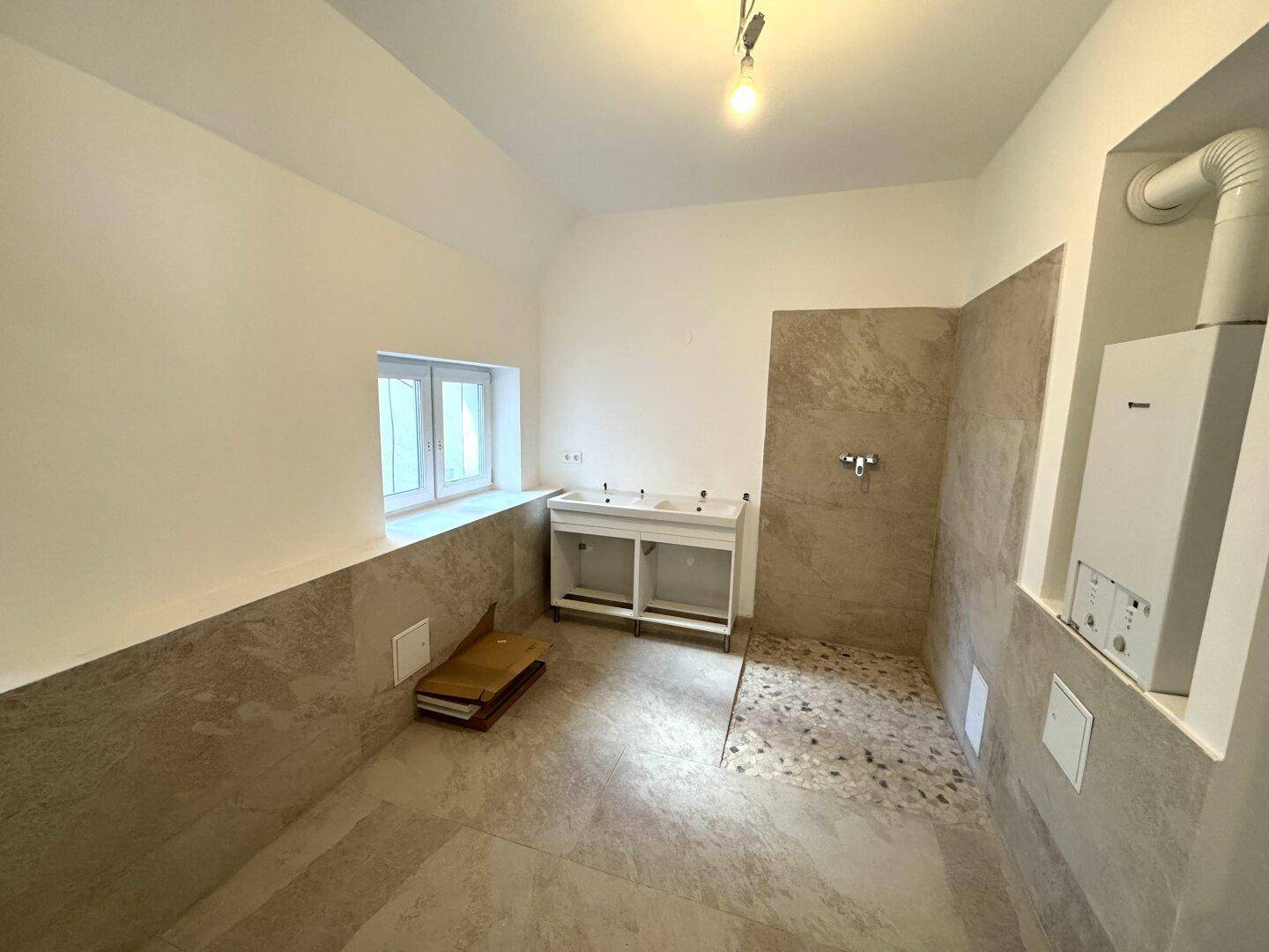 Badezimmer in Renovierung mit beigefarbenen Fliesen, vorbereitet für Doppelwaschbecken und Duschbereich.