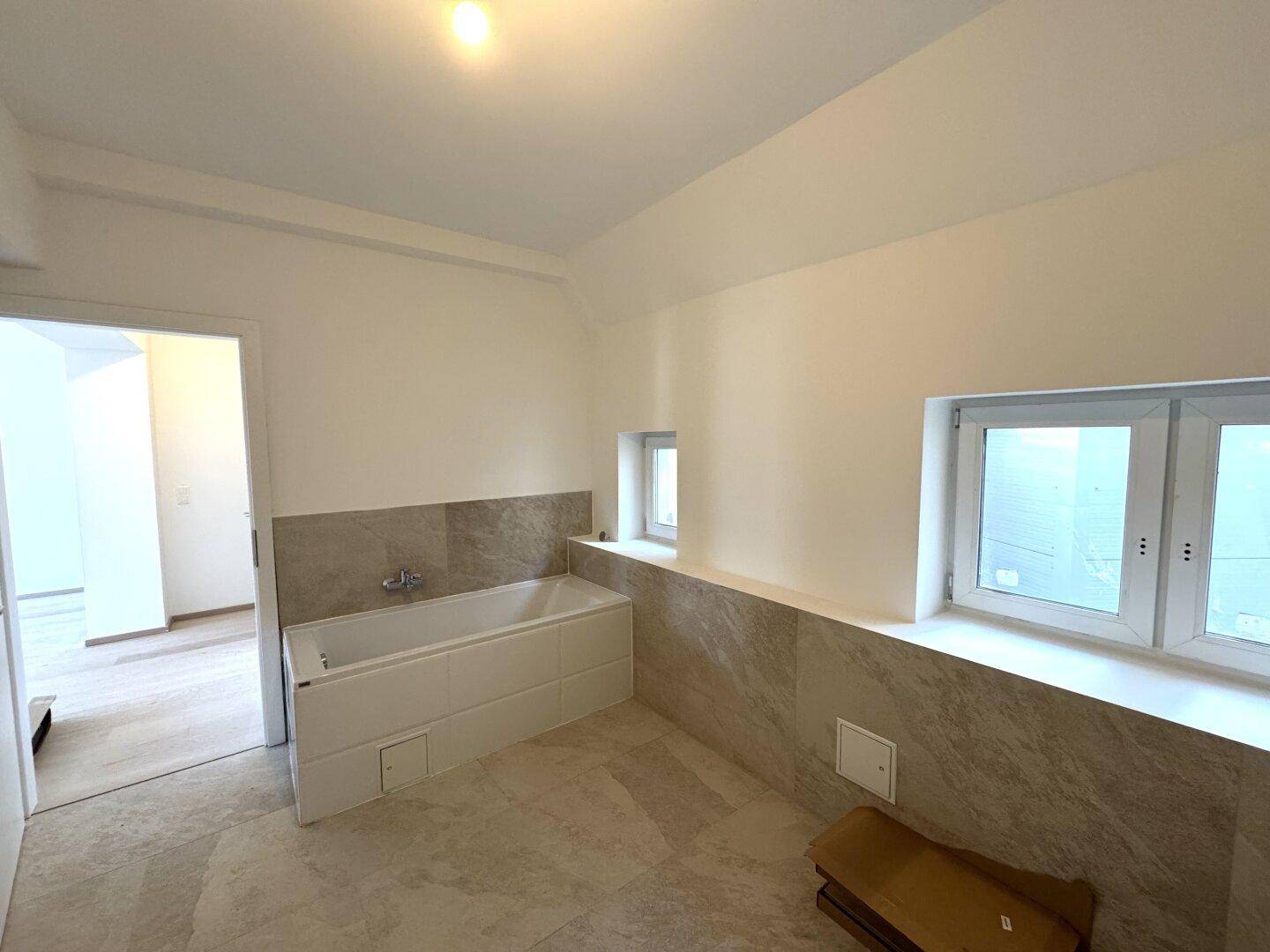 Badezimmer in Renovierung mit eingebauter Badewanne, beigefarbenen Fliesen und Fenstern für Tageslicht.