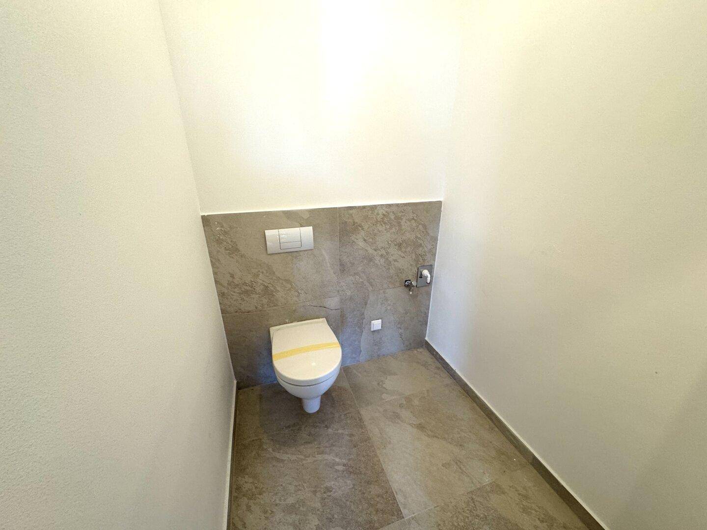 Modernes Gäste-WC mit wandhängender Toilette und eleganten grauen Fliesen an Wänden und Boden.