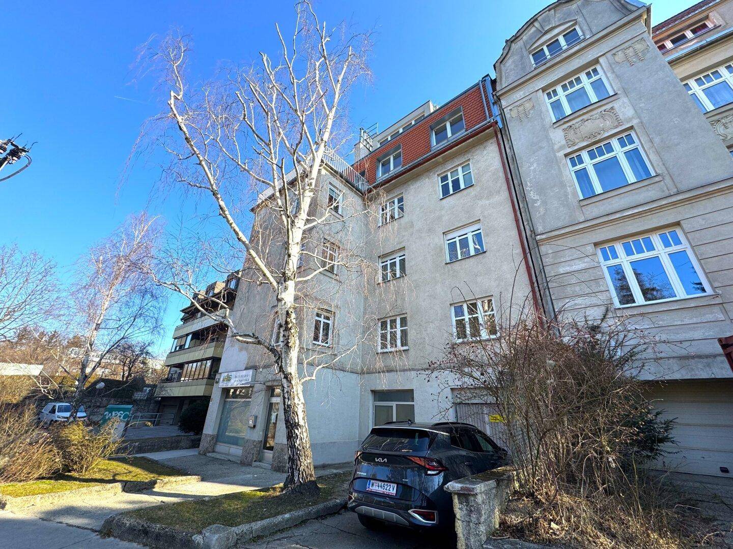 Seitenansicht des älteren Gebäudes mit geparktem Auto und Bäumen im Vordergrund.