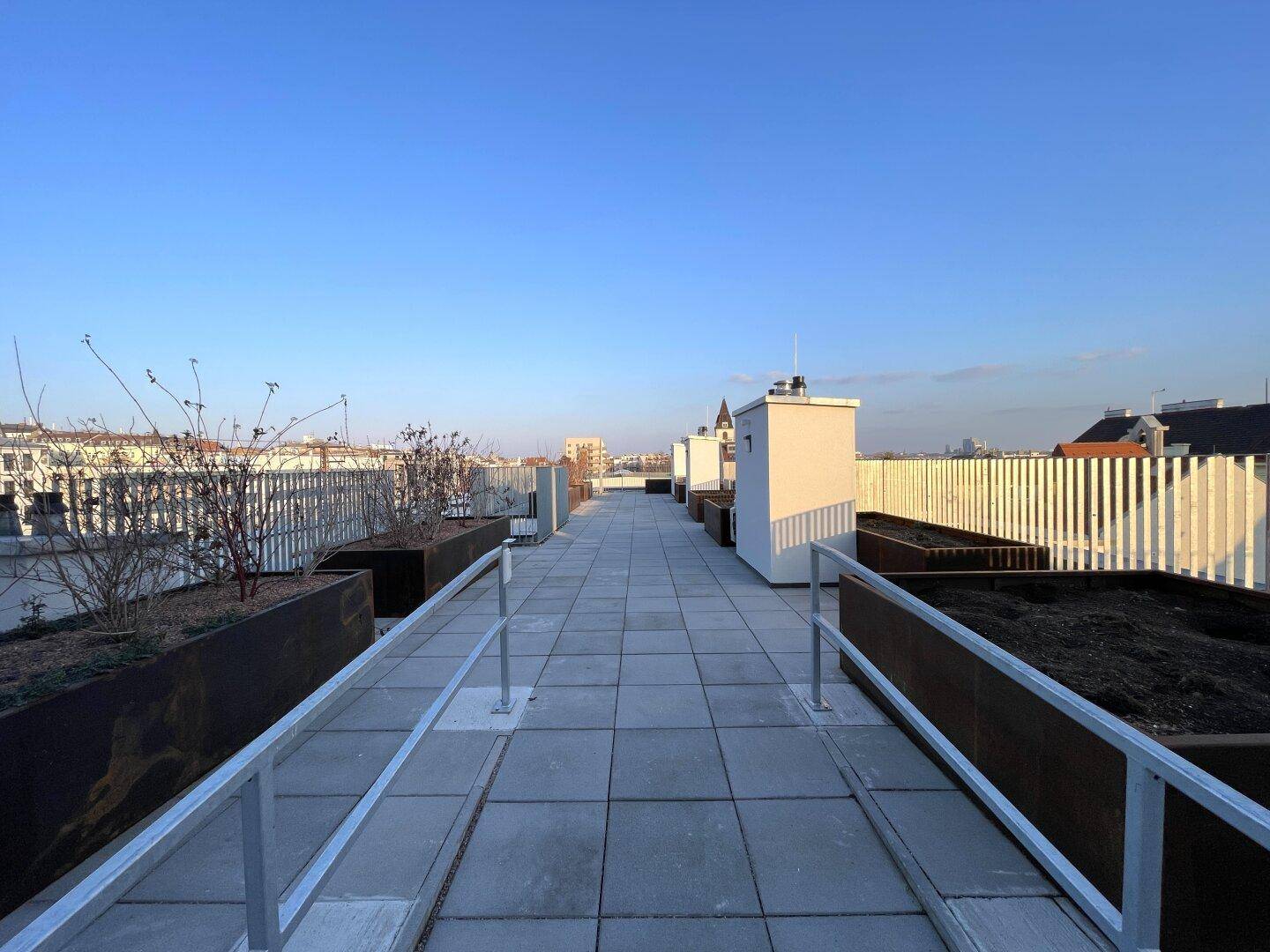 Weitläufige Dachterrasse mit Fliesenboden, Pflanzkübeln und Panoramablick über die Stadt.