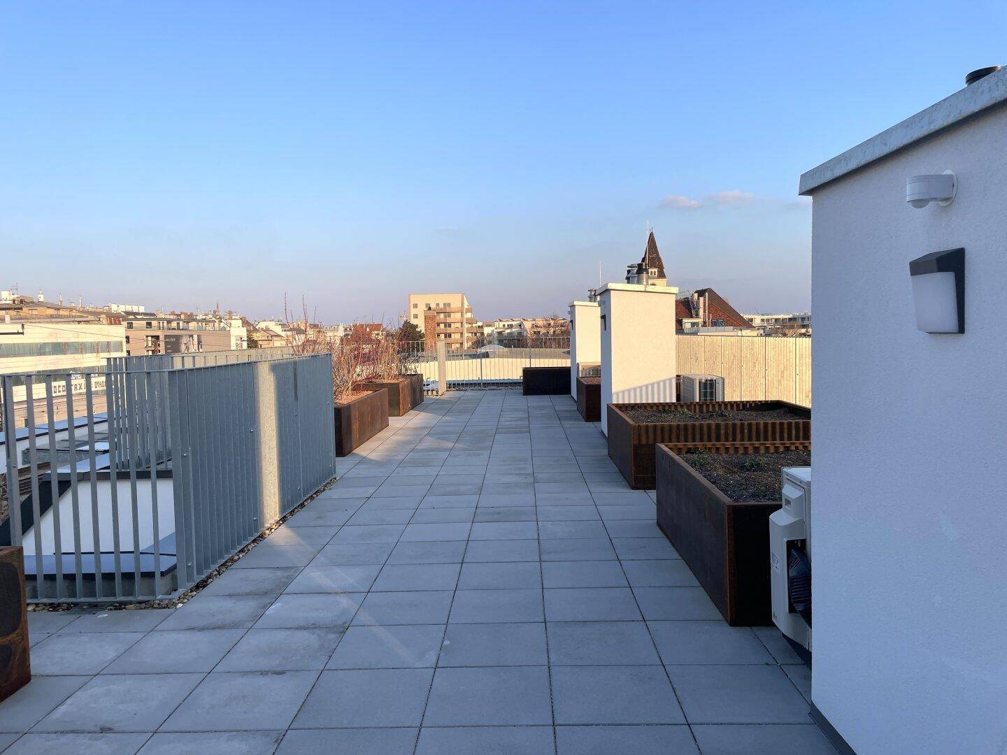 Geräumige Dachterrasse mit modernen Fliesen und Pflanzbereichen unter blauem Himmel.