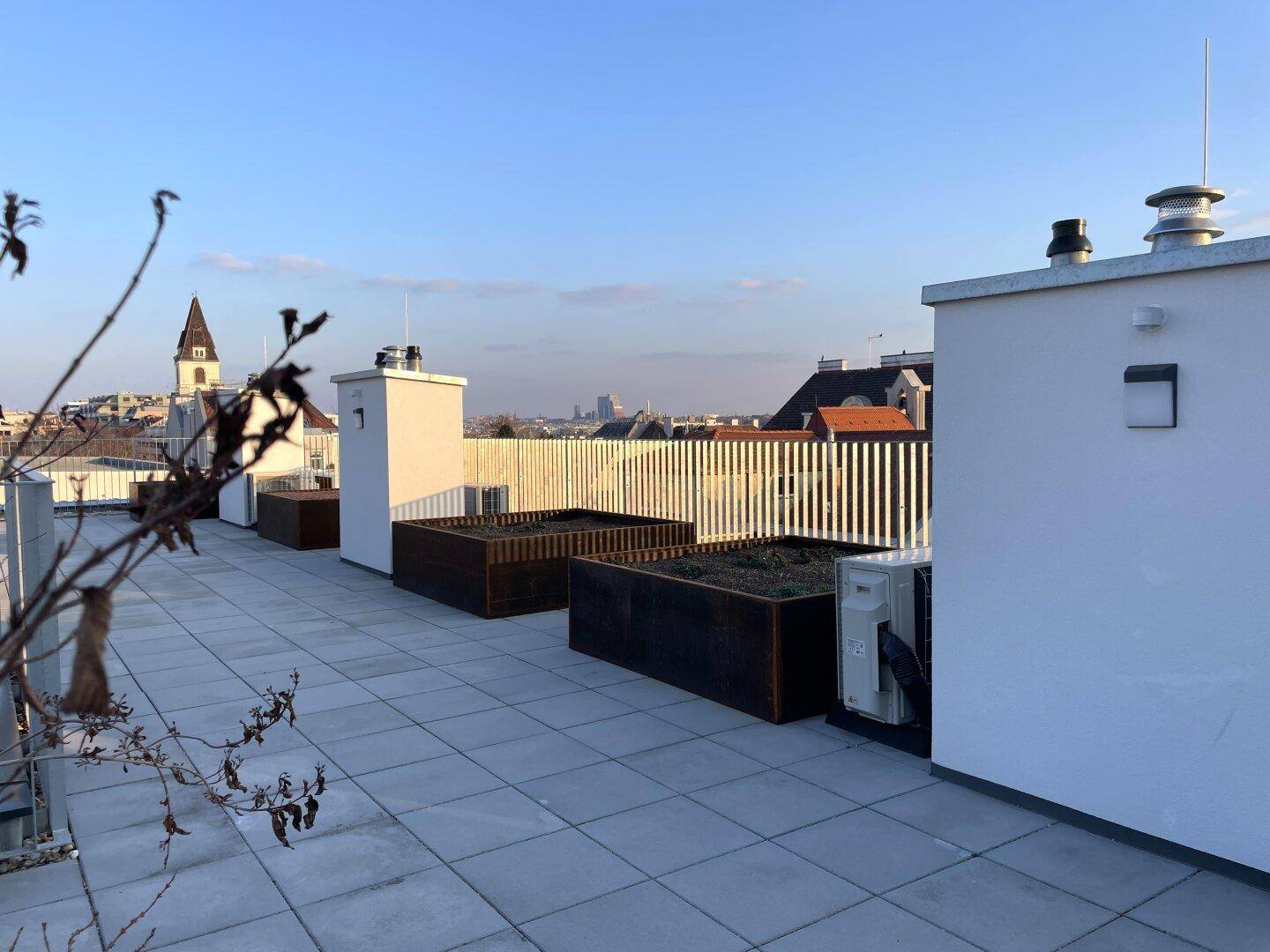 Dachterrasse mit Pflanzkübeln und weitem Blick auf die städtische Umgebung und den Horizont.