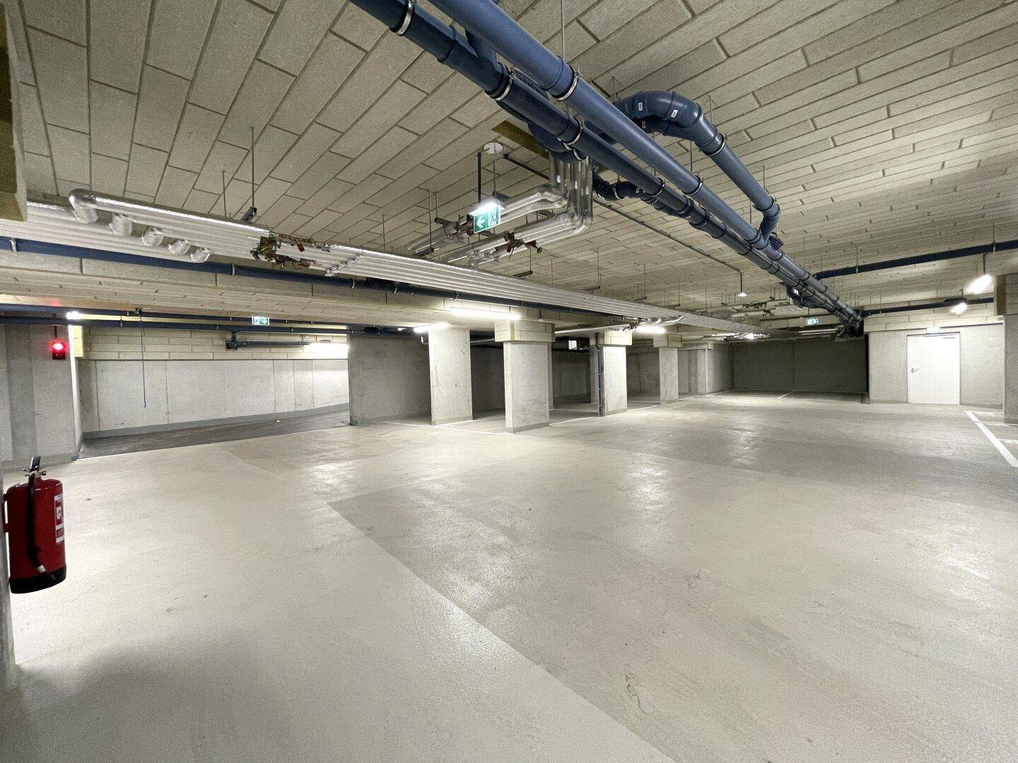 Helle Tiefgarage mit vielen Parkmöglichkeiten, Betonwänden und Deckeninstallationen.