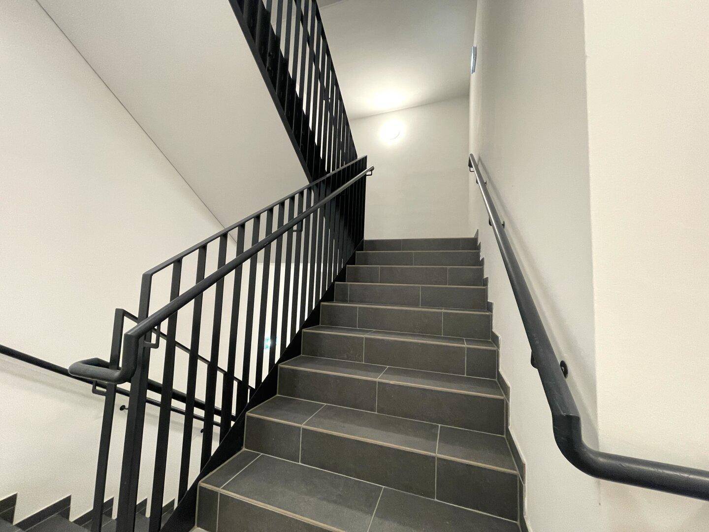 Modernes Treppenhaus mit grauen Fliesenstufen und elegantem schwarzen Metallgeländer.