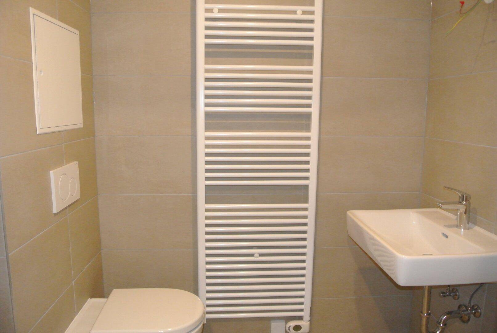 Modernes Badezimmer mit beigen Fliesen, wandhängendem WC, Waschbecken und beheiztem Handtuchhalter.