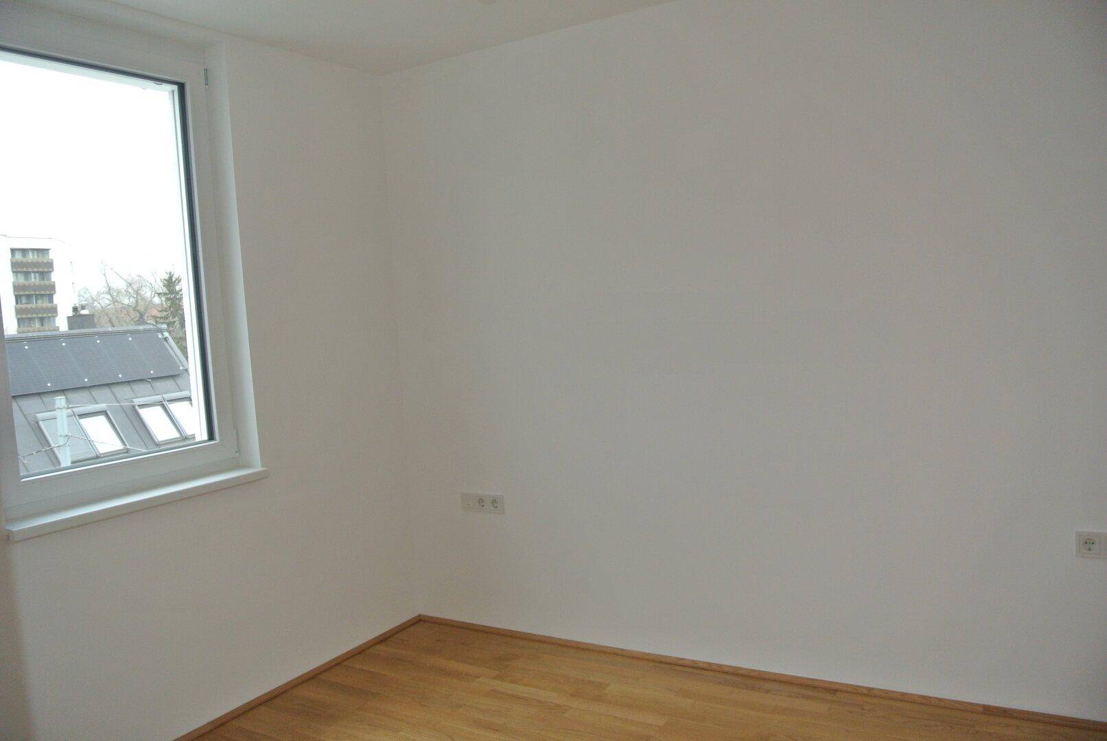 Helles Schlafzimmer mit Parkettboden und einem Fenster, das viel Tageslicht in den Raum lässt.