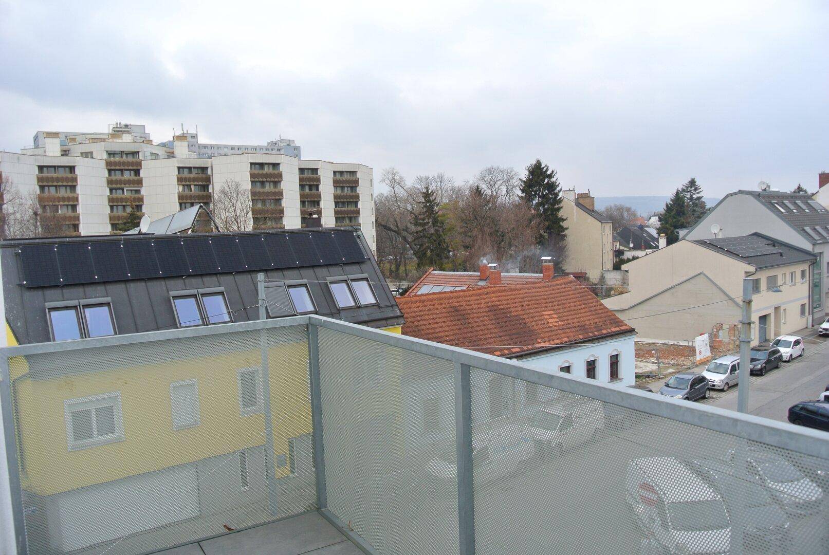 Aussicht von einem Balkon auf benachbarte Gebäude mit Solaranlagen und eine ruhige Wohnstraße.