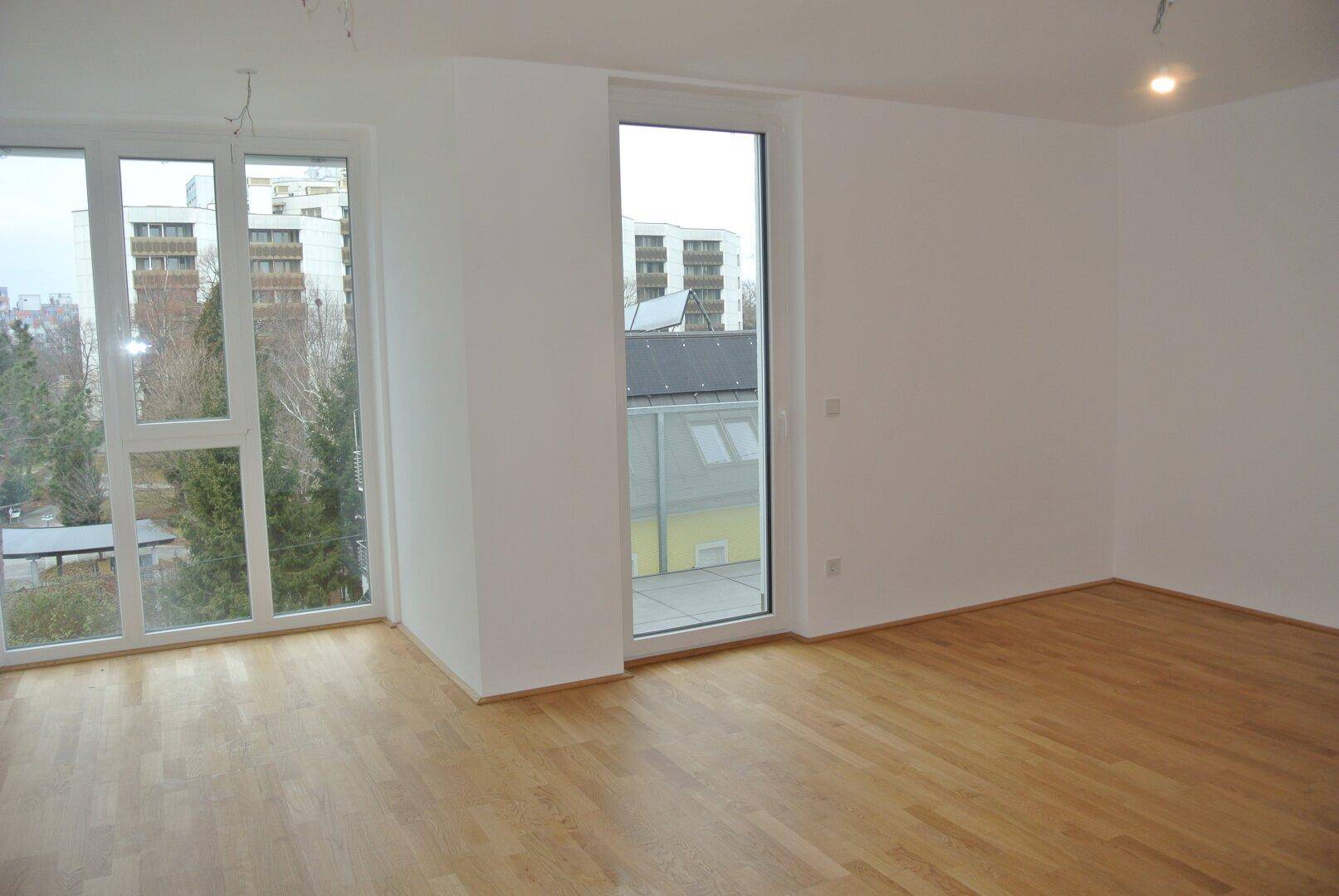 Heller, leerer Raum mit Holzboden und großen Fenstern, die viel Tageslicht hereinlassen.