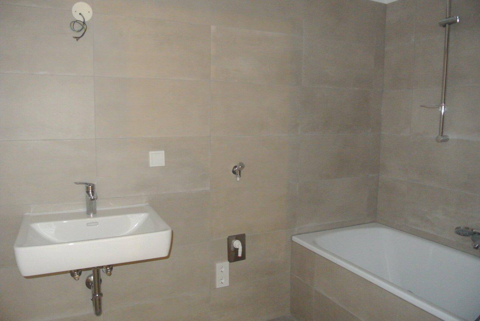 Modern gefliestes Badezimmer mit einem Waschbecken und einer Badewanne in neutralen Beigetönen.