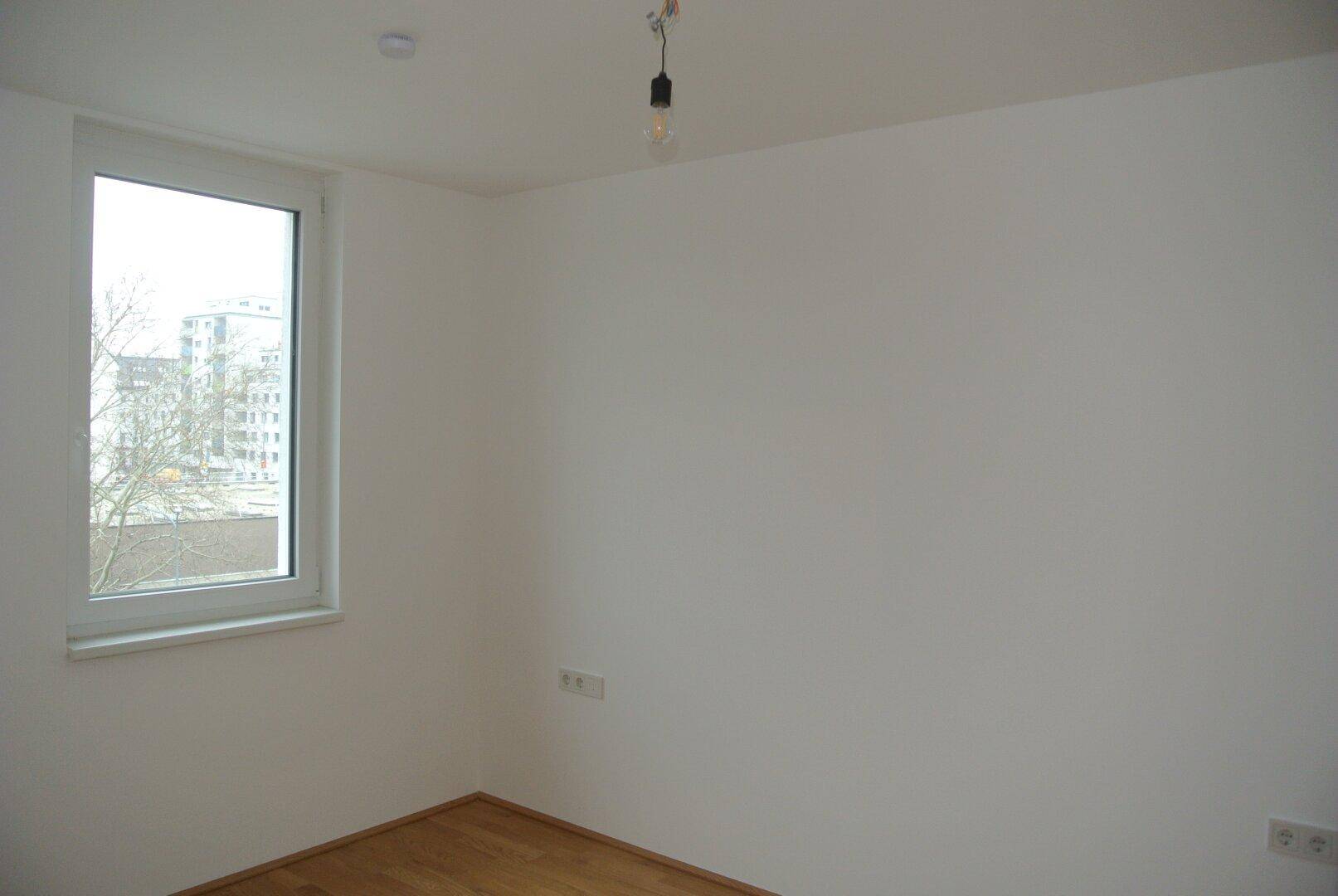 Leeres Schlafzimmer mit einem Fenster, das einen Blick auf die städtische Umgebung ermöglicht.