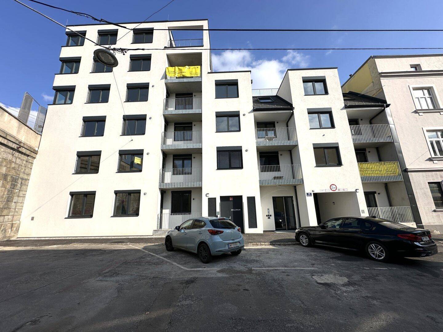 Moderne Wohnanlage mit weißer Fassade, Balkonen und Parkplätzen.