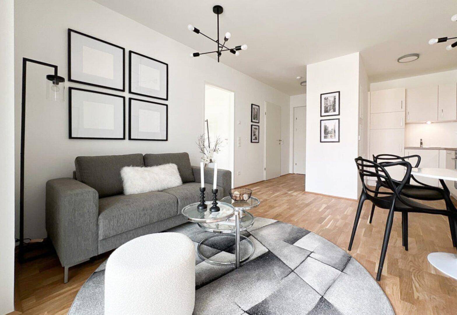 Gemütliches Wohnzimmer mit Sofa, Couchtisch und Holzboden, offen zu einer kleinen Küchenzeile.