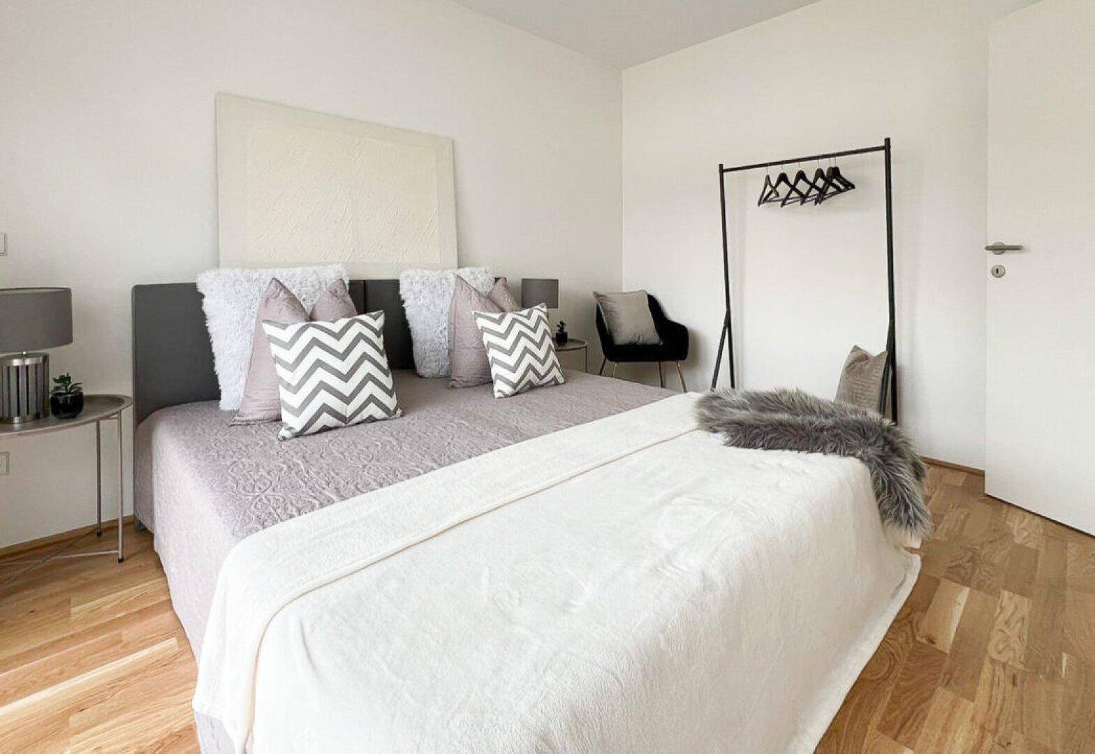 Helles Schlafzimmer mit Doppelbett, Holzboden und minimalistischer Einrichtung in Weißtönen.