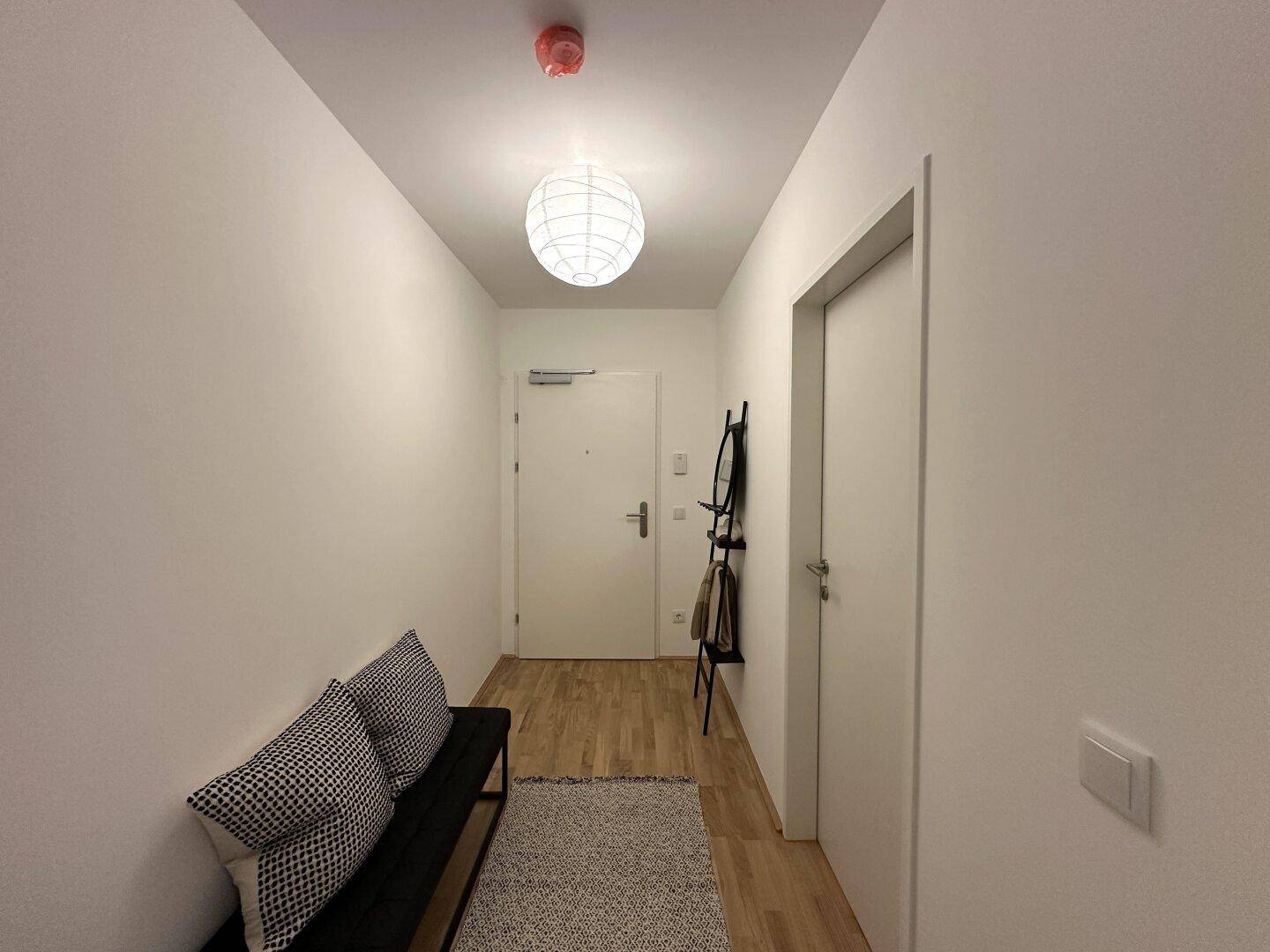 Heller Eingangsbereich mit Holzboden, Garderobe und moderner Deckenleuchte.