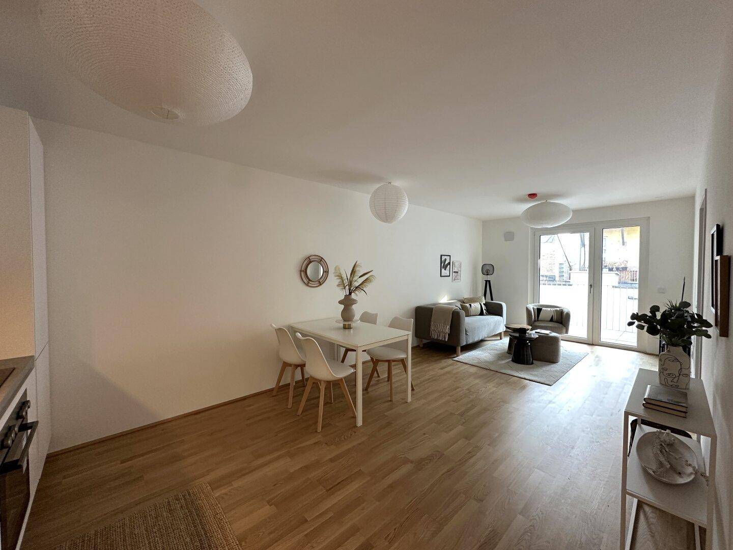 Geräumiger Wohn- und Essbereich mit hellem Holzboden und Zugang zum Balkon.