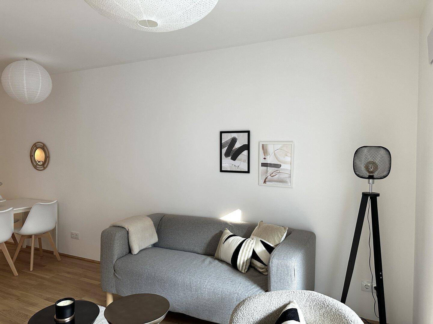 Gemütlicher Wohnbereich mit grauem Sofa, modernen Kunstwerken und Stehlampe.