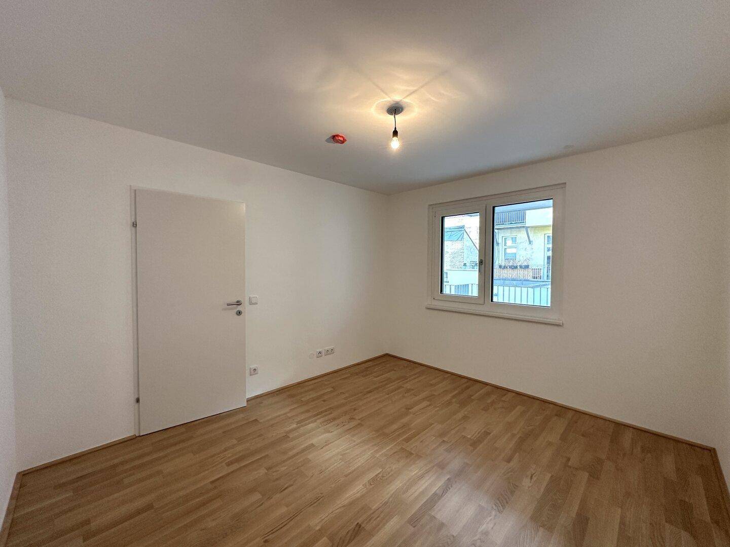 Unmöbliertes Schlafzimmer mit Holzboden und weißer Tür, bereit zur individuellen Gestaltung.