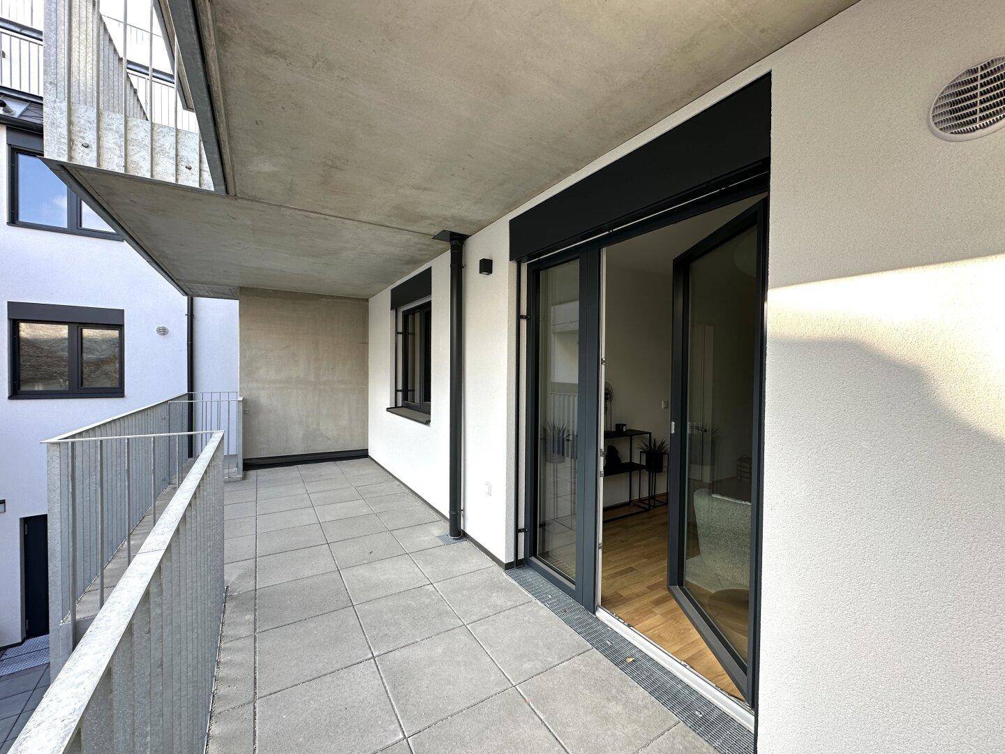 Heller Balkon mit Fliesenboden und Zugang zum Innenraum durch große Glastüren.