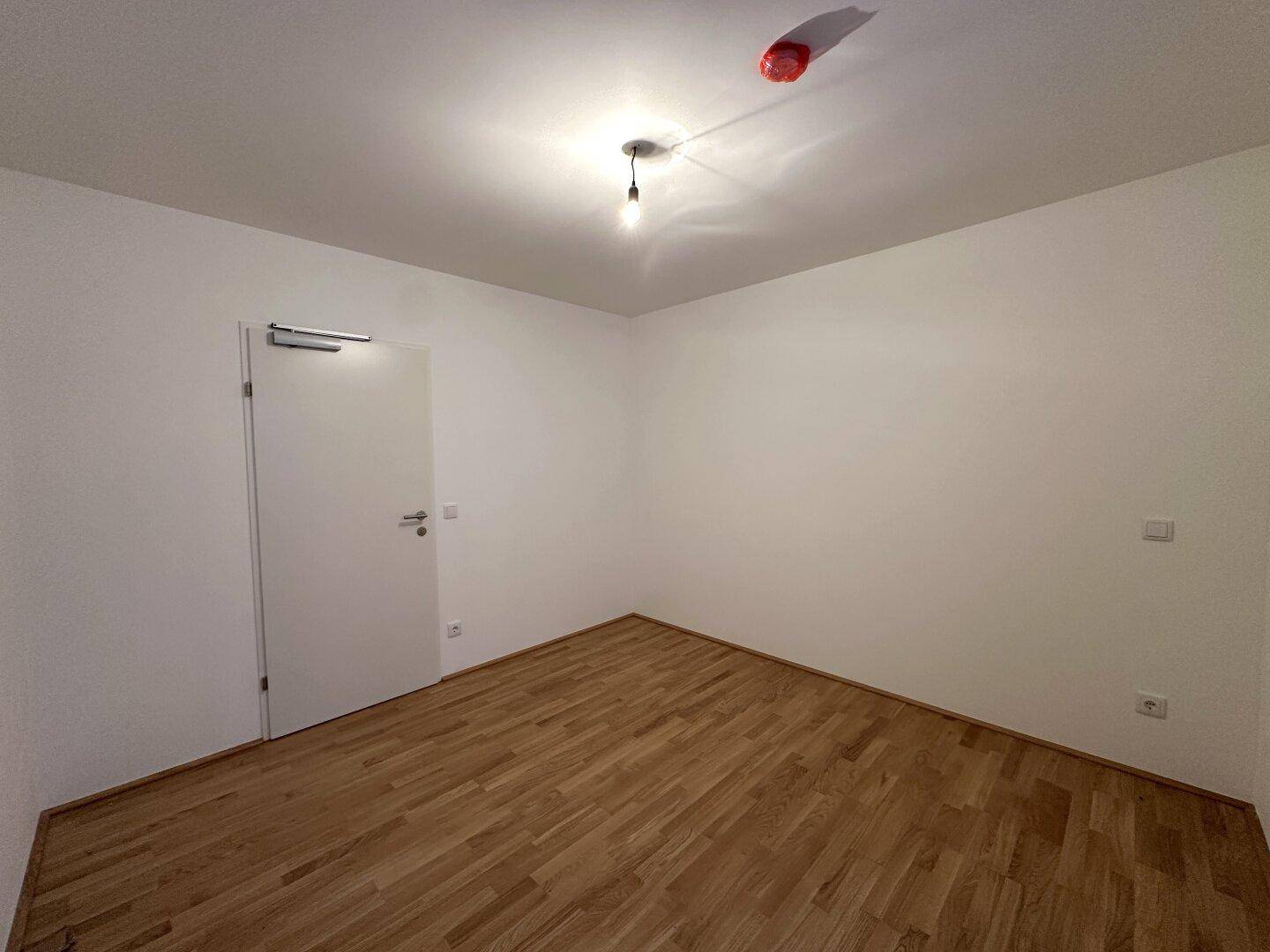 Unmöbliertes Zimmer mit Holzboden und weißer Tür, bereit zur individuellen Einrichtung.
