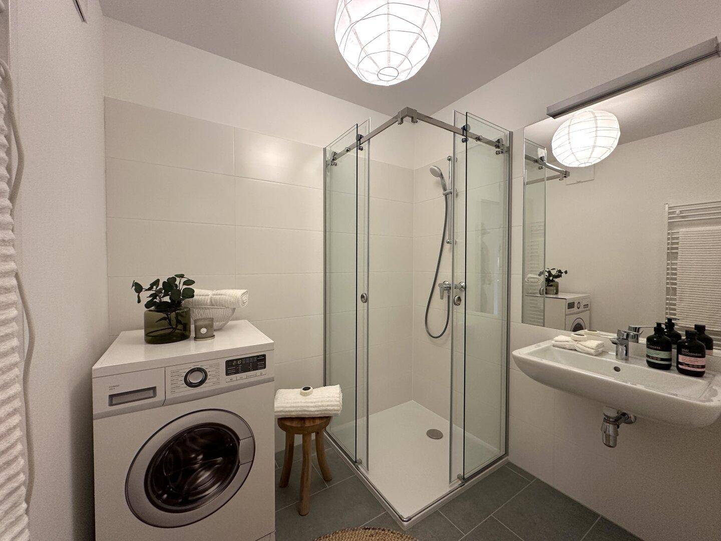 Modernes Badezimmer mit Dusche, Waschmaschine und beheiztem Handtuchhalter.
