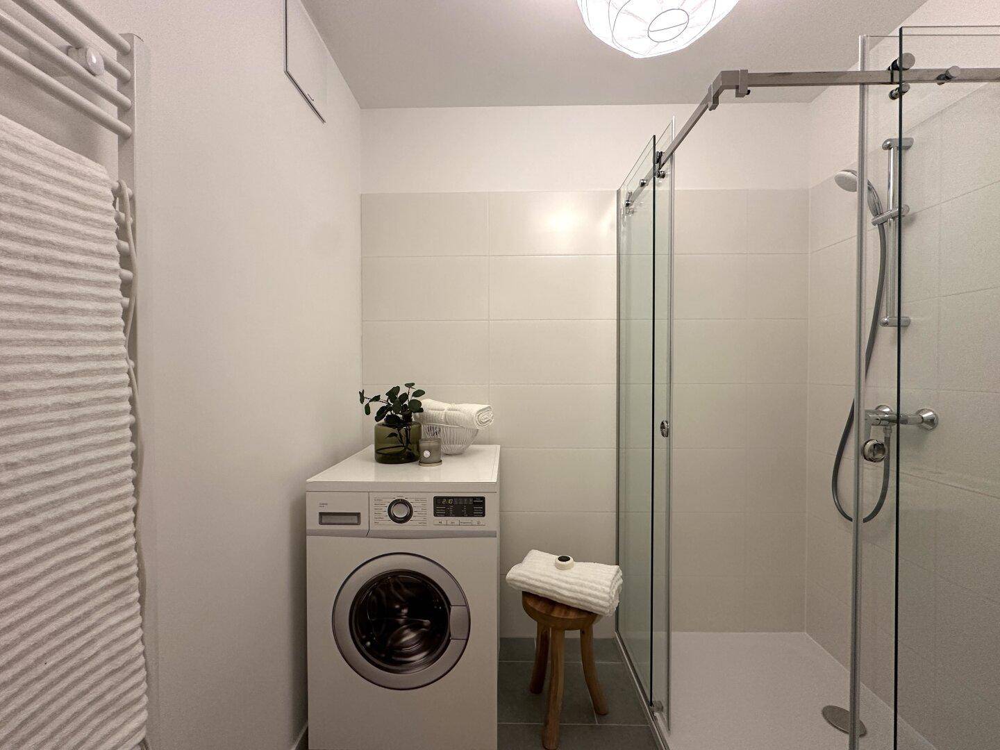 Modernes Badezimmer mit Duschkabine, Waschmaschine und Handtuchheizkörper.
