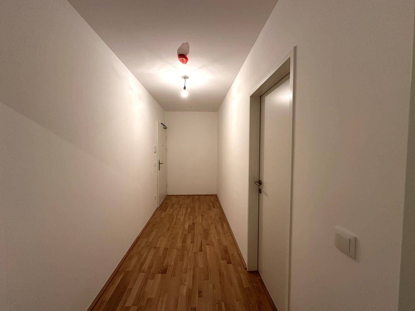Heller Flur mit Parkettboden und weißen Wänden, verbindet die Wohnbereiche.