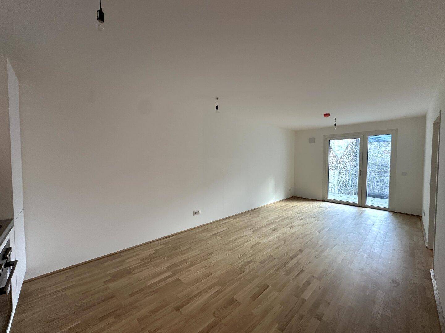 Offener Wohnbereich mit Parkettboden und viel Tageslicht durch die Balkontür.