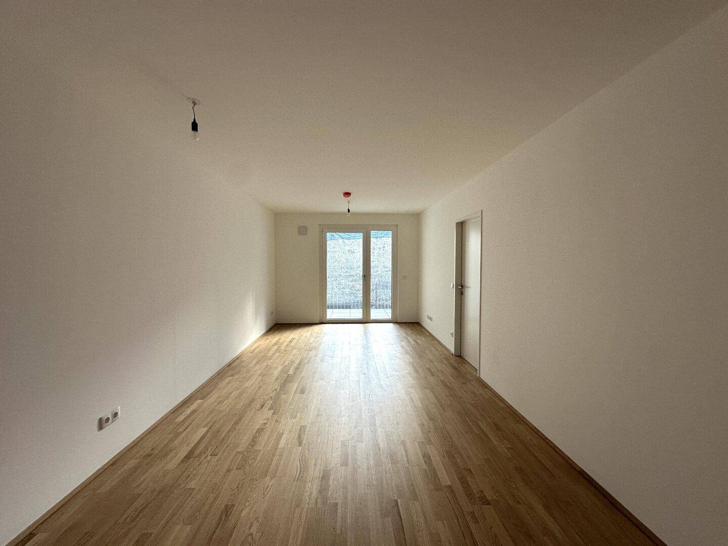 Geräumiger, heller Wohnraum mit Parkettboden und Zugang zu einem Balkon.