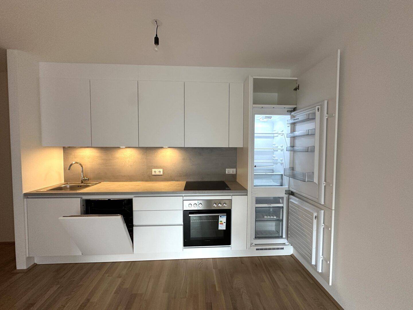 Moderne Küchenzeile mit weißen Schränken, integrierten Geräten und Holzboden.