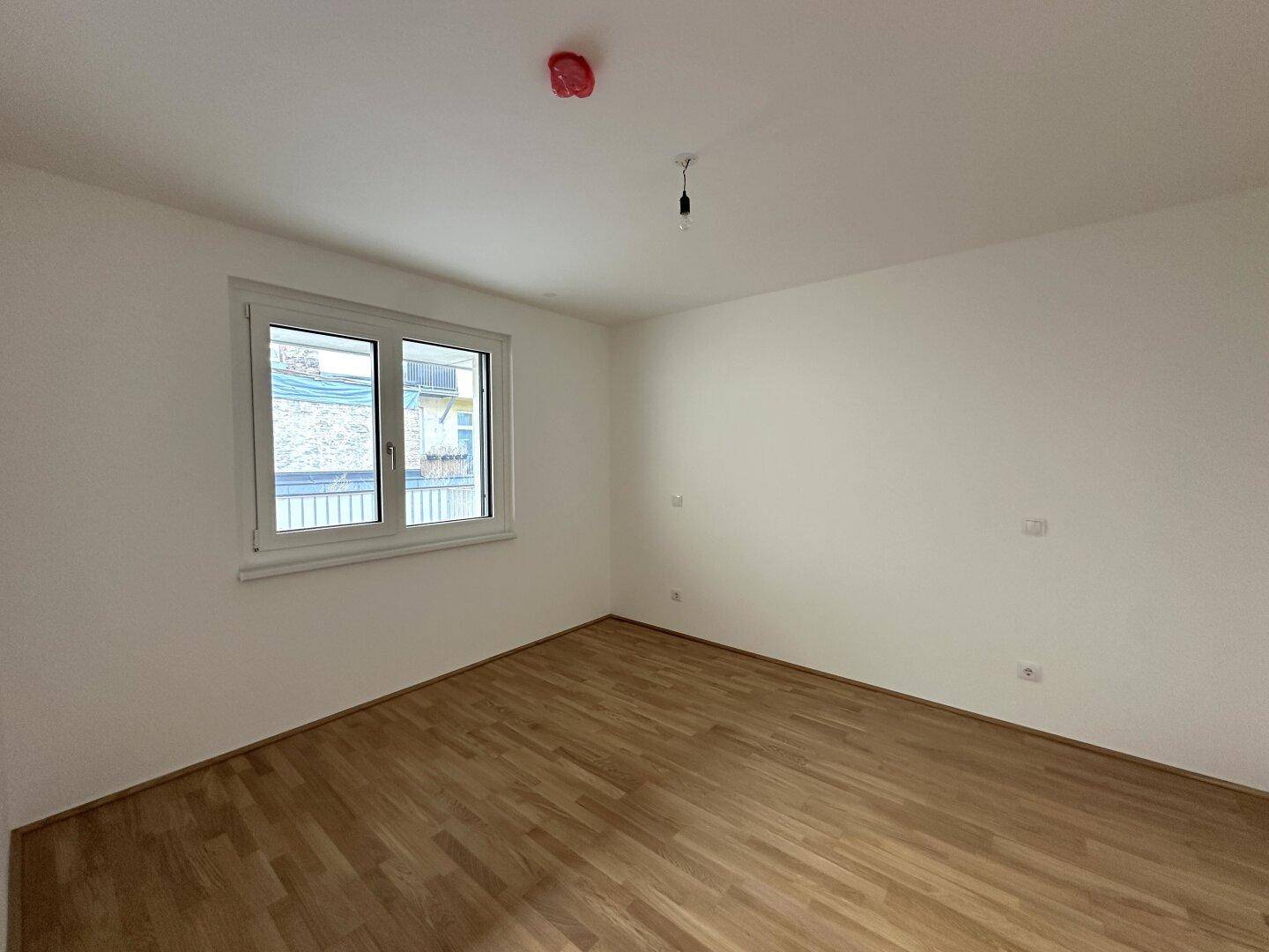 Helles Schlafzimmer mit Parkettboden und einem großen Fenster für viel Tageslicht.