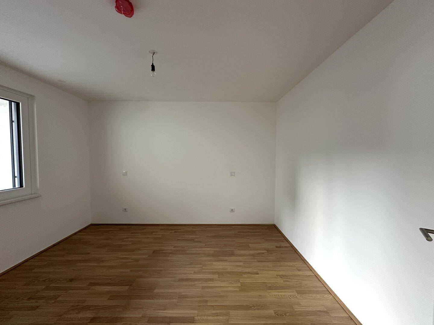 Leeres Zimmer mit Parkettboden und weiß gestrichenen Wänden, bereit zur Einrichtung.