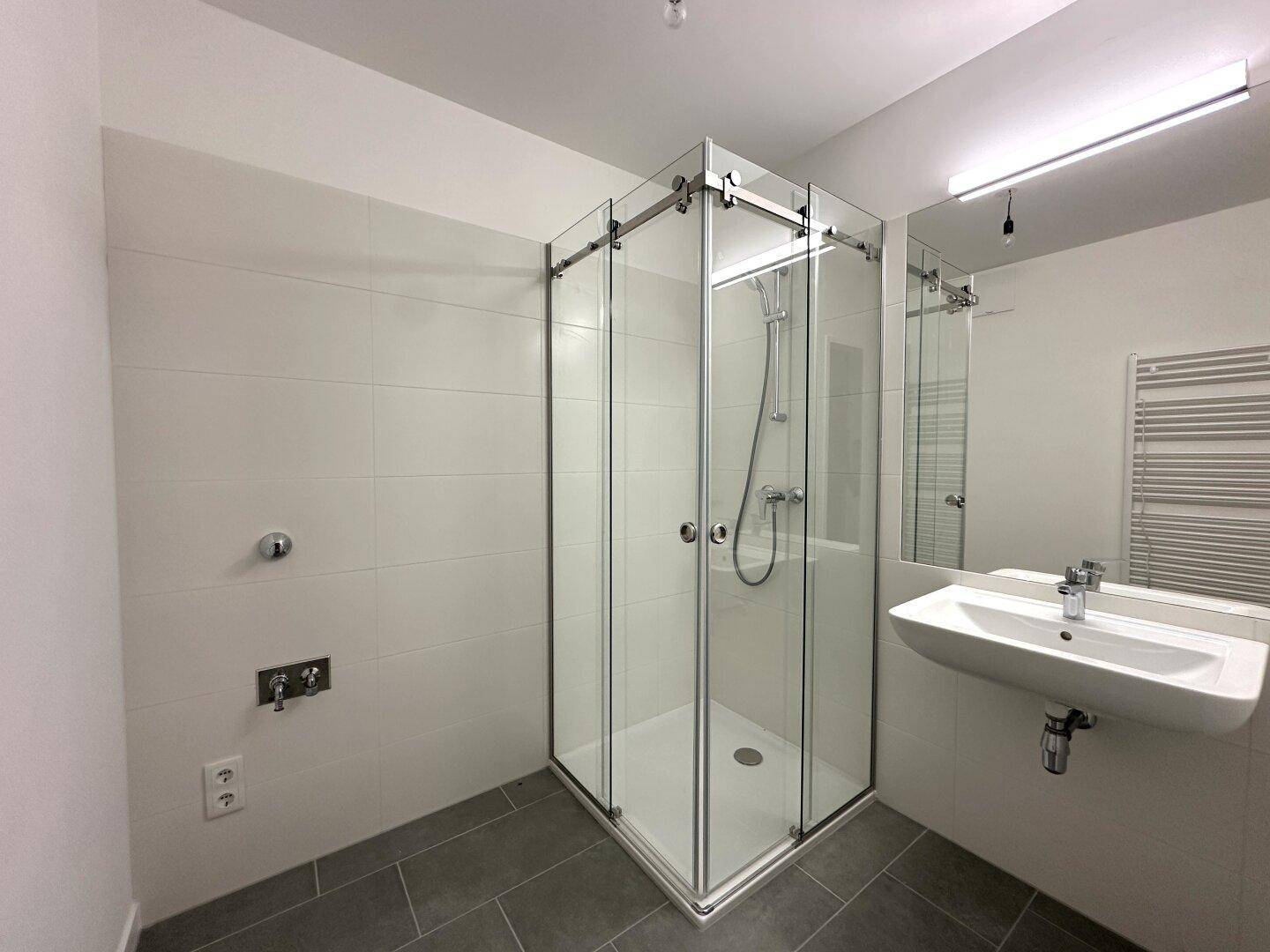 Modernes Badezimmer mit Duschkabine, Waschbecken und beheiztem Handtuchhalter.