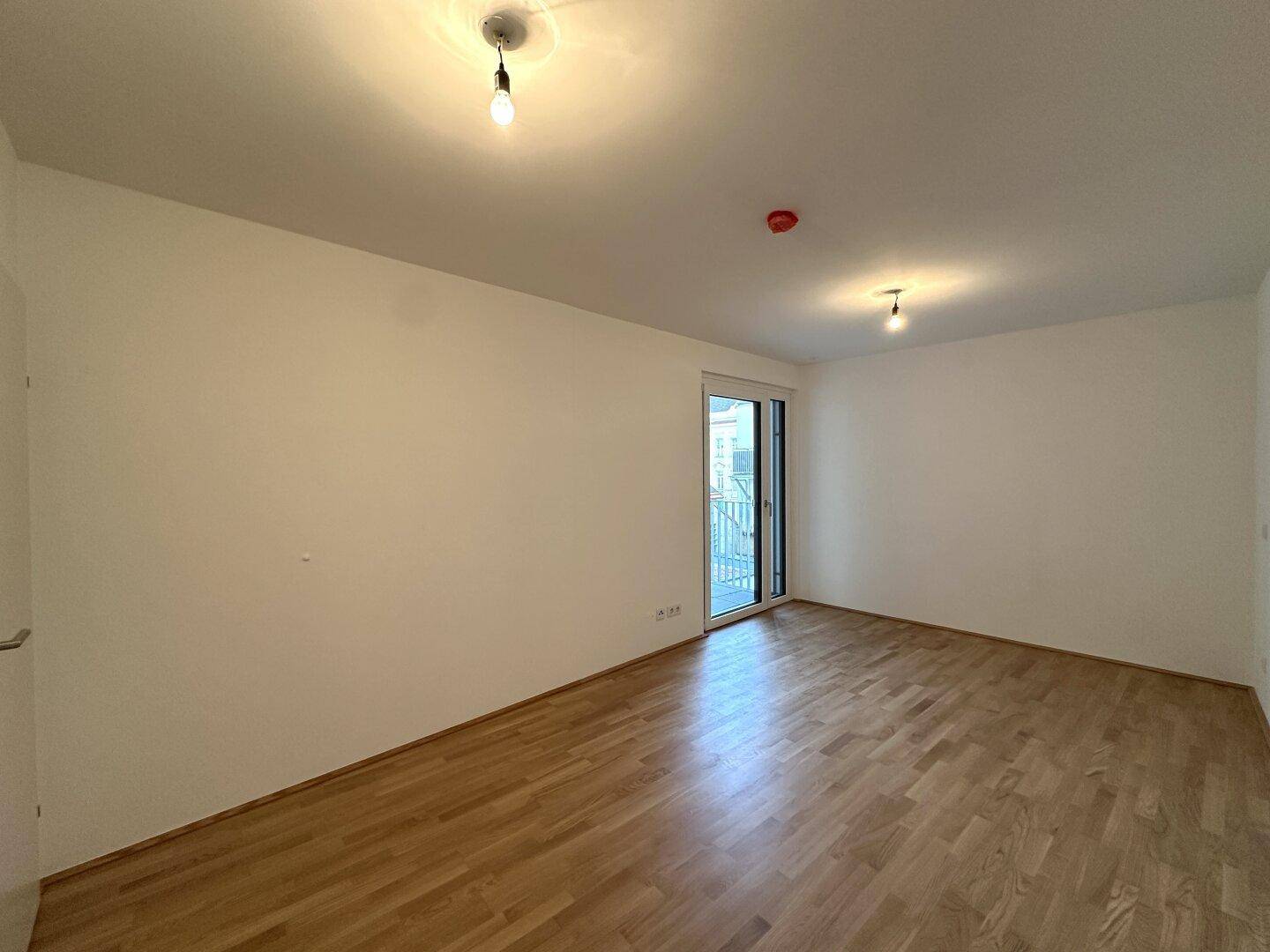 Helles Schlafzimmer mit Parkettboden und Zugang zu einem kleinen Balkon.