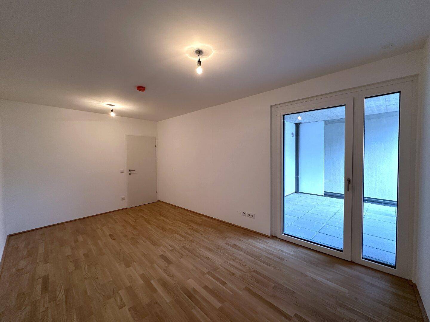 Geräumiges Zimmer mit Parkettboden und großen Fenstern zum Außenbereich.
