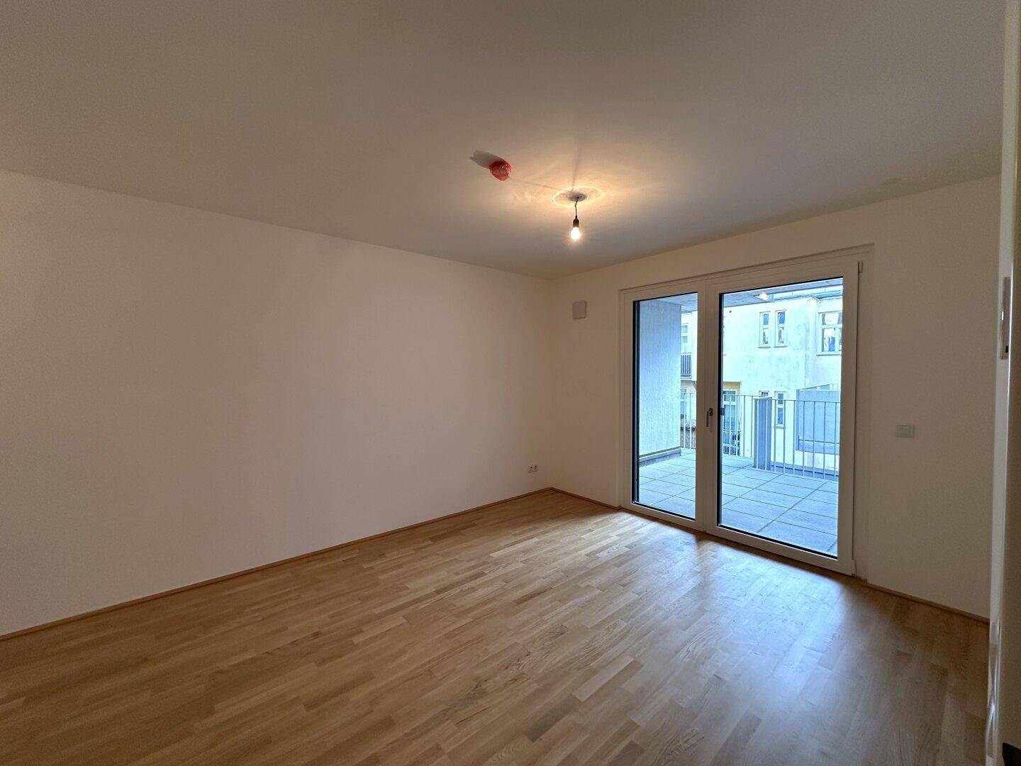 Lichtdurchfluteter Wohnraum mit Holzboden und großen Fenstern zum Balkon.
