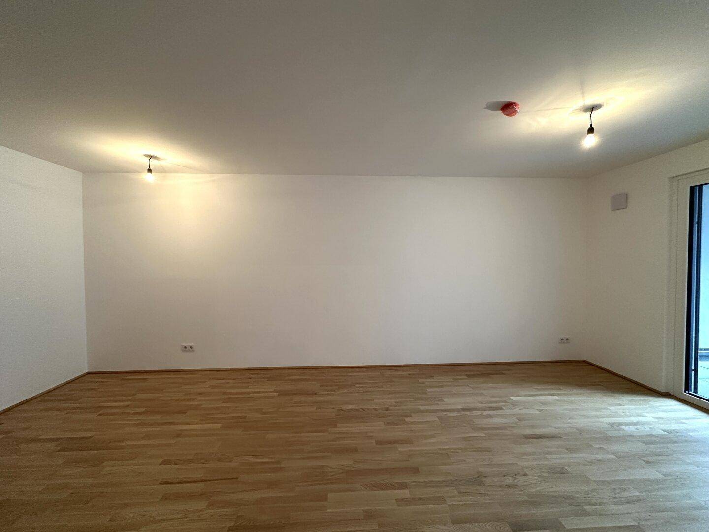 Weiter Blick in den leeren Wohnbereich mit hellem Parkettboden und weißen Wänden.