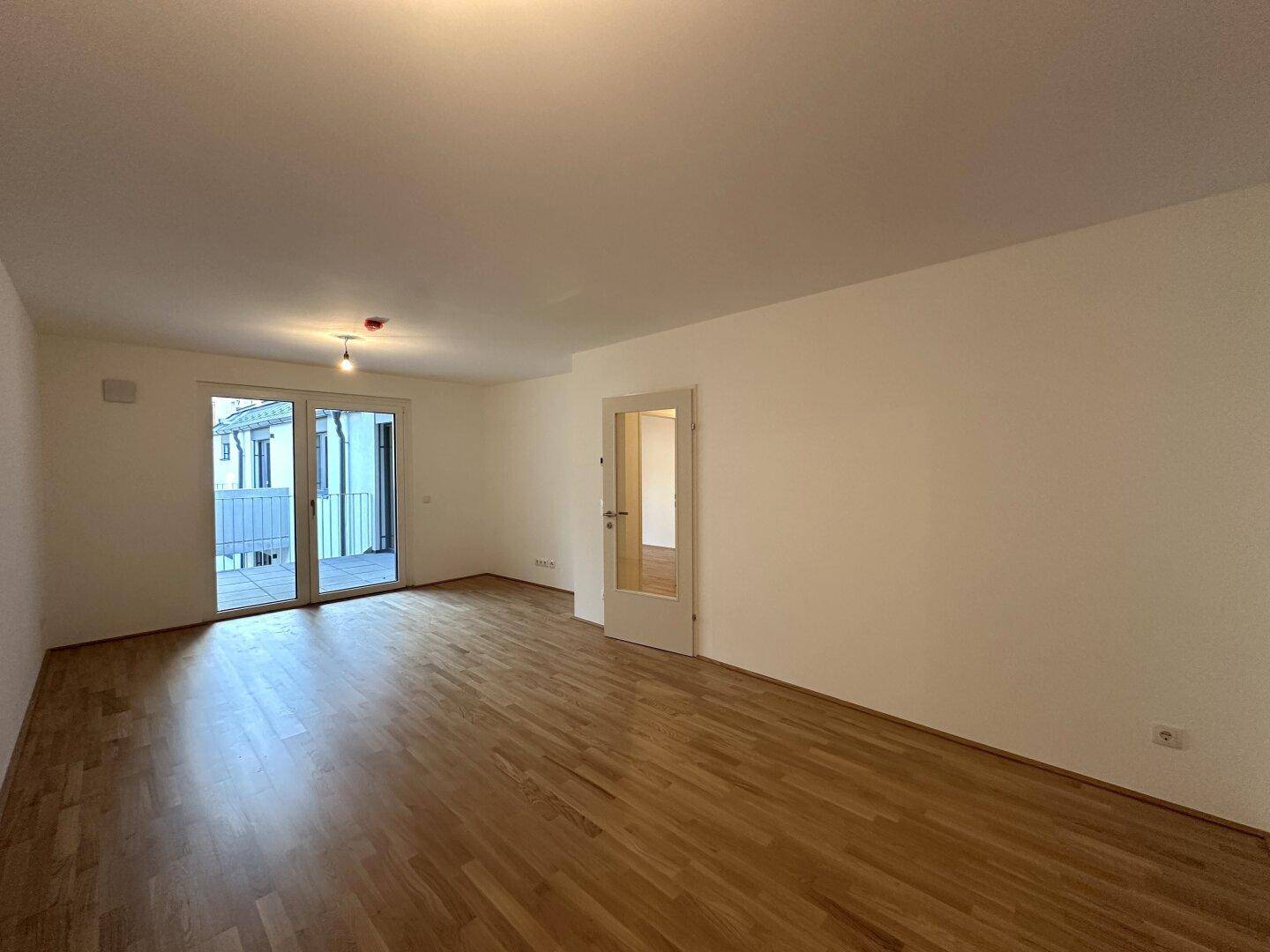 Geräumiger Wohnbereich mit Parkettboden und Zugang zu einem Balkon.