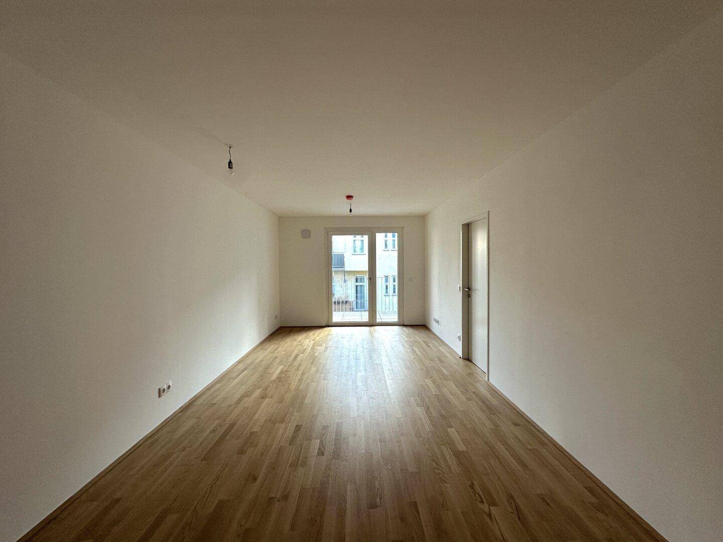 Geräumiger Wohnbereich mit Parkettboden und Zugang zu einem Balkon, ideal für individuelle Gestaltung.