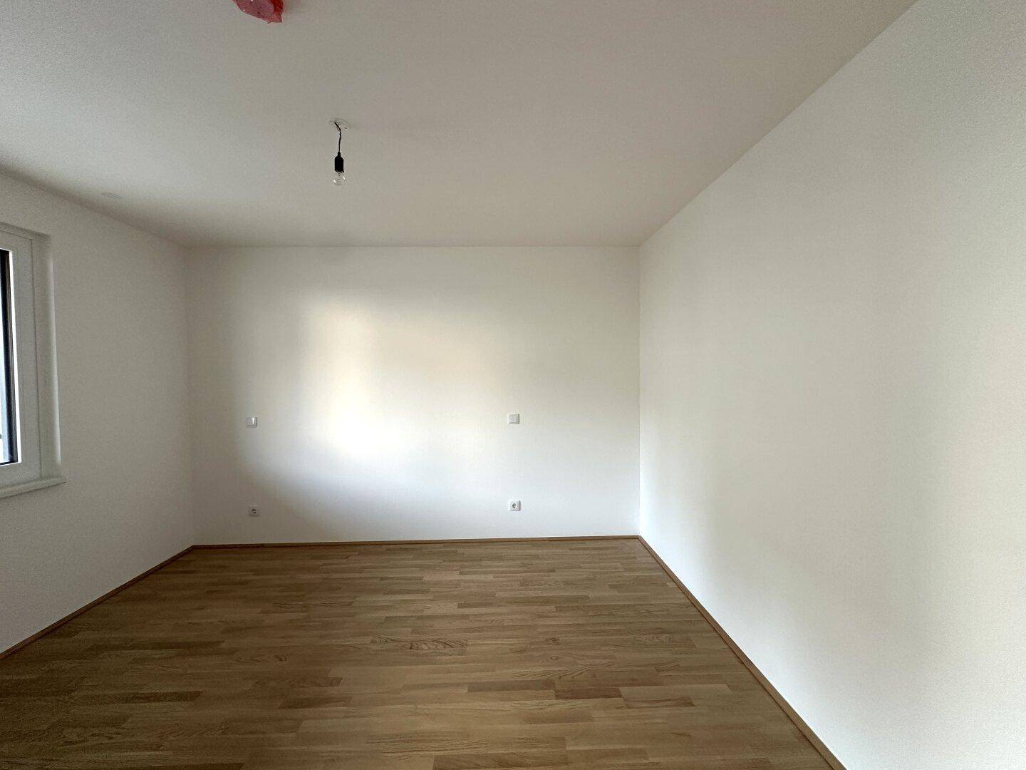 Helles Schlafzimmer mit Parkettboden und einem Fenster, bietet eine ruhige Atmosphäre.