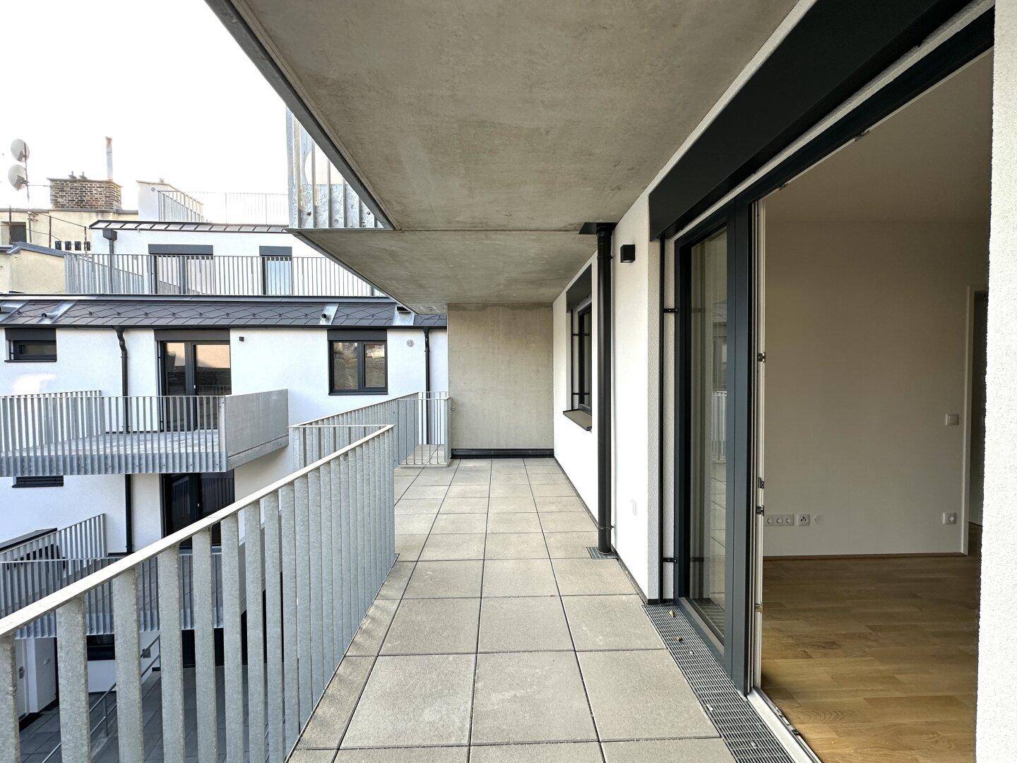 Langer Balkon mit Fliesenboden und Metallgeländer, bietet Platz für Entspannung im Freien.