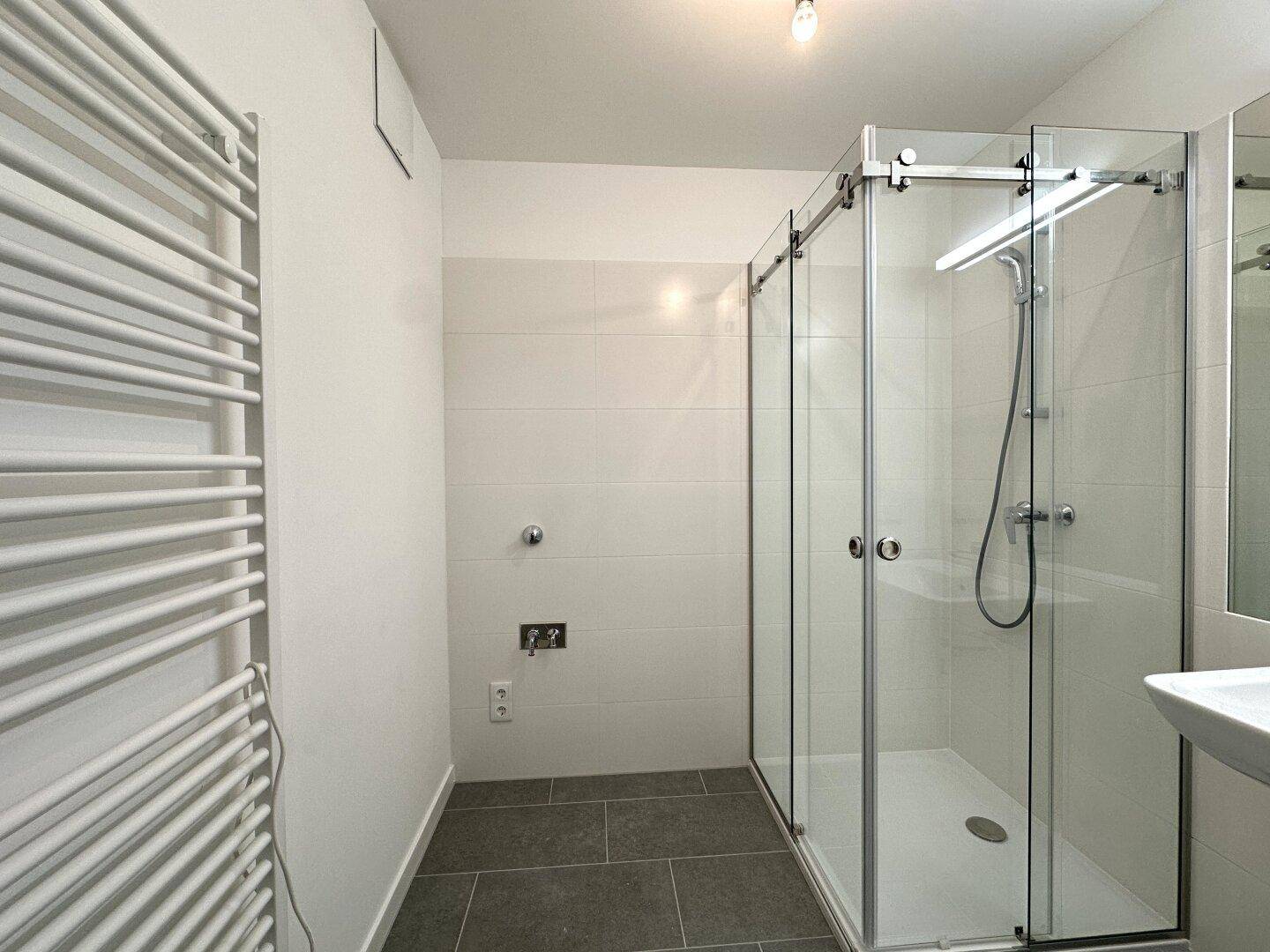Helles Badezimmer mit Duschkabine, Fliesenboden und praktischem Handtuchheizkörper.